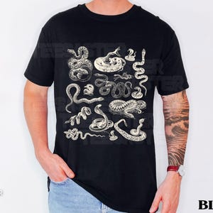 May include: Black t-shirt with a detailed print of various snake illustrations. The snakes are shown in different positions, with a vintage, engraved aesthetic. The word "BLACK" is printed in white, bold letters, indicating the shirt's colour.