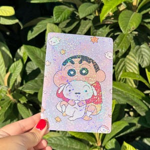 Puede incluir: Una pegatina holográfica rectangular con una ilustración de dibujos animados de un niño de pelo oscuro con camiseta roja y pantalones cortos amarillos, abrazando a un perro blanco pequeño sobre un fondo morado claro con estrellas.