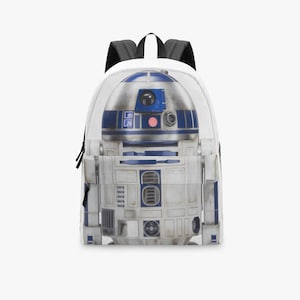 Peut inclure: Un sac à dos blanc avec une image détaillée du personnage de Star Wars R2-D2. Le sac à dos présente un design bleu et blanc, avec des bretelles noires et une poignée supérieure. Le design est un gros plan du corps du droïde.