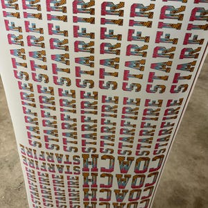 May include: A sheet of printed stickers with the words "STARFIRE" and "COACH" in a repeating pattern. The text is in a bold, stylized font with pink, blue, and gold accents. The background is white.