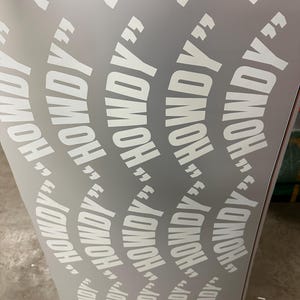 May include: A light gray surface with a repeating pattern of the word "HOWDY" in white, enclosed in quotation marks. The text is arranged in curved lines, creating a dynamic visual effect.