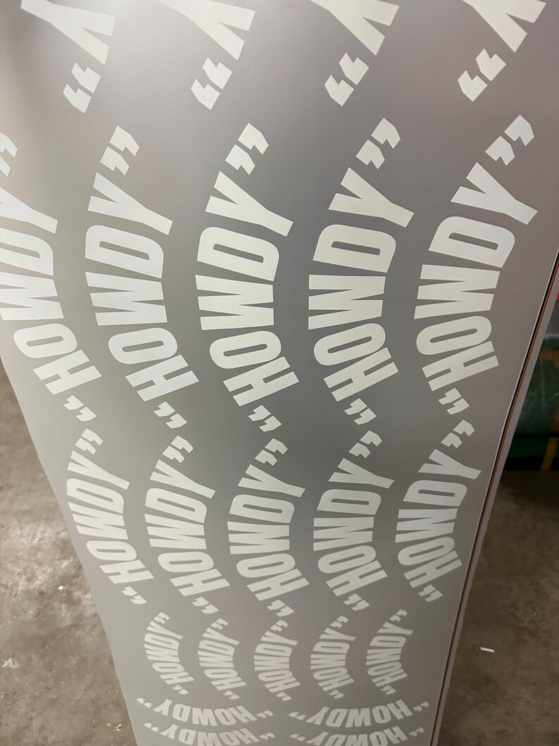 May include: A light gray surface with a repeating pattern of the word "HOWDY" in white, enclosed in quotation marks. The text is arranged in curved lines, creating a dynamic visual effect.