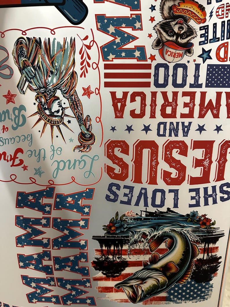 May include: A white sheet with patriotic designs. The sheet features the Statue of Liberty, the words "America" and "Jesus," and a raccoon with a hotdog. The words "Land of the Free" and "Mama" are also visible.