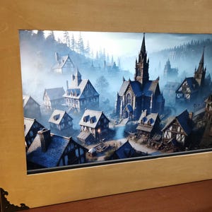 Puede incluir: Una ilustración digital de un pueblo medieval con una gran iglesia en el centro. El pueblo está rodeado de árboles y niebla. La imagen se muestra en un marco de madera.