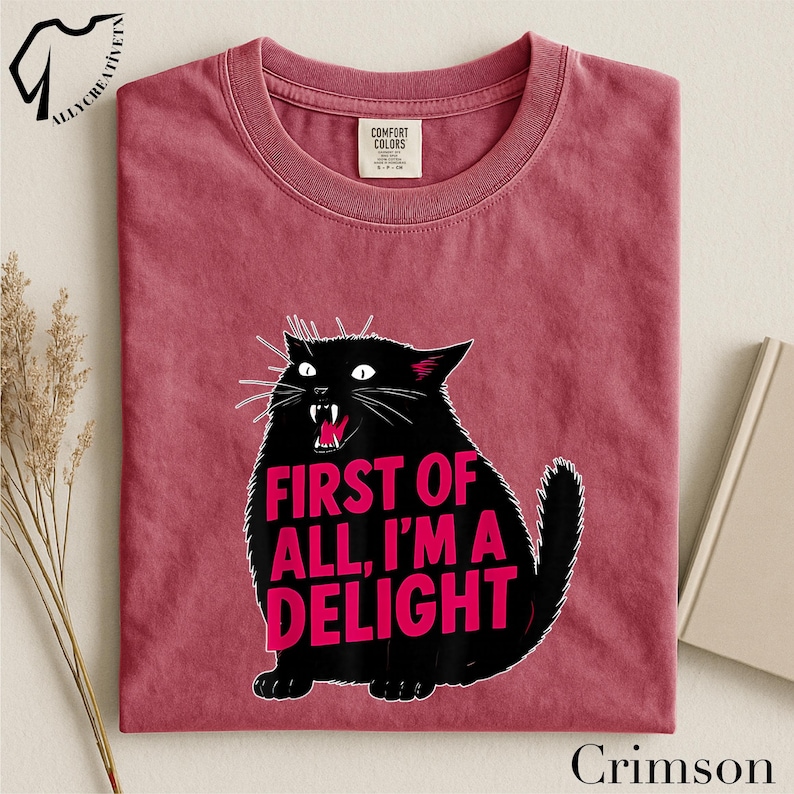 A red t-shirt with a graphic design of a black cat and the text "FIRST OF ALL, I'M A DELIGHT" printed on it.