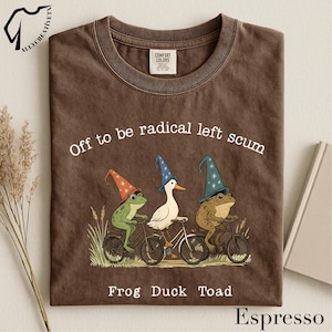 May include: Espresso-colored t-shirt with the text "Off to be radical left scum" and a graphic of a frog, duck, and toad riding bicycles, each wearing a wizard hat. The words "Frog Duck Toad" are below the graphic.
