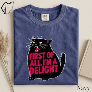 A navy blue t-shirt with a graphic design of a black cat with the text "FIRST OF ALL, I'M A DELIGHT" printed on it.