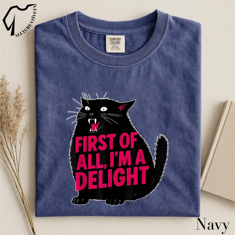 A navy blue t-shirt with a graphic design of a black cat with the text "FIRST OF ALL, I'M A DELIGHT" printed on it.