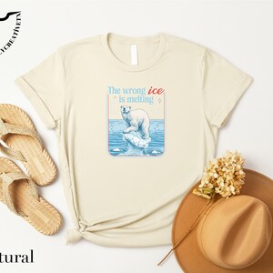 a beige t-shirt with a graphic design, a pair of flip-flops, a hat, and some flowers, all arranged on a white background.
