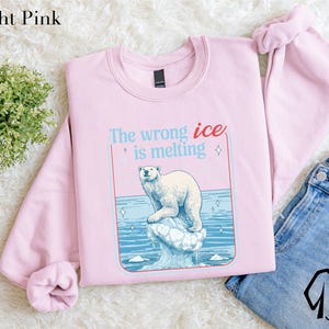 A pink sweatshirt with a graphic of a polar bear on a melting ice floe, accompanied by the text "The wrong ice is melting".