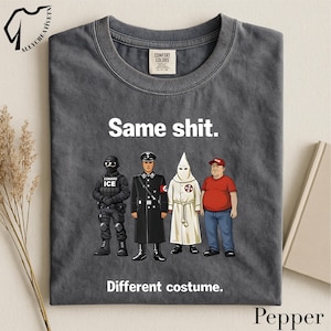 May include: Dark gray t-shirt with the text "Same shit. Different costume." and illustrations of four figures in different uniforms and attire. The shirt has a crew neck and a Comfort Colors tag.