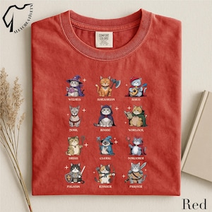May include: Red t-shirt featuring a grid of illustrated cats in various fantasy roles, including Wizard, Barbarian, and Fighter. The text "ALLYCREATIVETN" is in the upper left corner, and "Red" is at the bottom right. The shirt is made of a soft material.