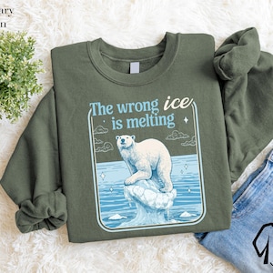 a green sweatshirt with a graphic design depicting a polar bear on a melting ice floe, accompanied by the text "The wrong ice is melting".