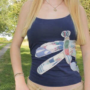 May include: A navy blue vest top featuring a large, multi-patterned fabric appliqué in the shape of a dragonfly. The dragonfly design is constructed from various small patches of fabric with different colours and prints, including floral and striped motifs.