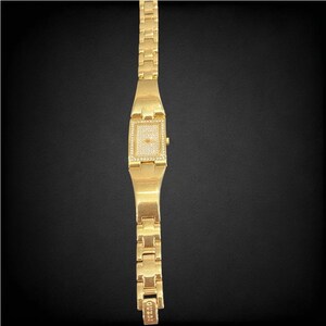 Pu&ograve; includere: Un orologio Guess dorato con un quadrante quadrato e un design a cristalli simili a diamanti. L'orologio ha un cinturino in metallo dorato.