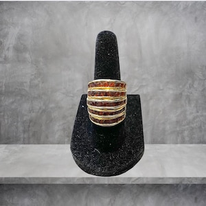 May include: A gold ring with multiple bands of brown gemstones. The ring is displayed on a black ring holder.