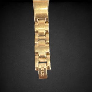 Pu&ograve; includere: Cinturino da orologio dorato con una chiusura che recita "GUESS".
