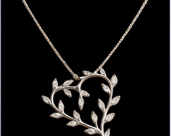 Può includere: Una collana d'argento con un ciondolo a forma di cuore che presenta un delicato design di rami intrecciati con foglie incastonate con pietre preziose trasparenti.