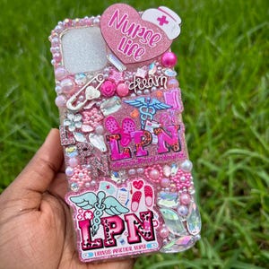 May include: A pink and white bedazzled phone case with the words "Nurse Life" in a heart shape. The case is decorated with pink pearls, rhinestones, and the letters "LPN". Additional embellishments include a nurse's hat, medical symbols, and the word "dream".