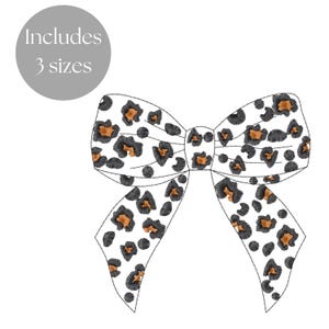 May include: A white bow with a leopard print design. The bow is made of fabric and has a black outline. The bow is tied in a knot and the ends are hanging down.