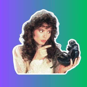 Puede incluir: Una mujer con un vestido blanco y una corona en la cabeza señala a una criatura alienígena negra con múltiples patas.