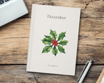 May include: A cream-colored notebook with the word "December" printed at the top. A watercolor illustration of holly with red berries is centered on the cover. The text "Ilex aquifolium" is printed at the bottom.