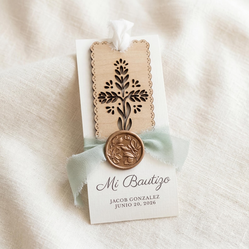 May include: A rectangular white card featuring a laser-cut wooden cross topper with scalloped edges, a sage green frayed ribbon, and a circular bronze wax seal with a floral design. The card displays the text Mi Bautizo, Jacob Gonzalez, June 20, 2026.