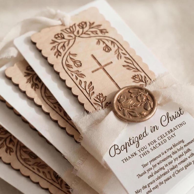 May include: A stack of rectangular baptism favor tags featuring light wood cutouts with scalloped edges, engraved with a cross and floral arch. Each tag is tied with cream-colored ribbon and a bronze-toned wax seal with a floral design.