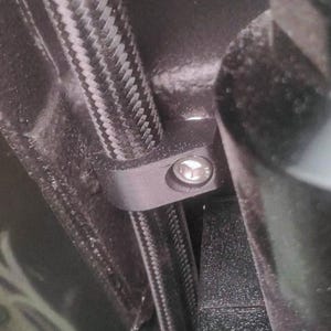 May include: Close-up of a black and silver hose clamp attached to a black braided hose. The clamp has a single screw.
