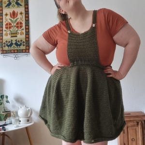 以下が含まれることがあります： 茶色のトップスとストラップが付いた緑色のクロシェドレス。ドレスはフレアスカートで、シンプルなステッチパターンで作られています。