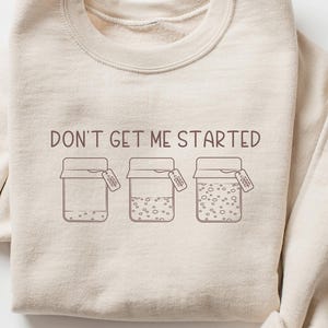 May include: A beige sweatshirt with the text "DON'T GET ME STARTED" and a graphic of three jars with lids.