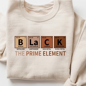 May include: A beige sweatshirt with a graphic print of the word "BLACK" spelled out using the chemical symbols for boron, lanthanum, carbon, and potassium. The text "THE PRIME ELEMENT" is printed below the chemical symbols.