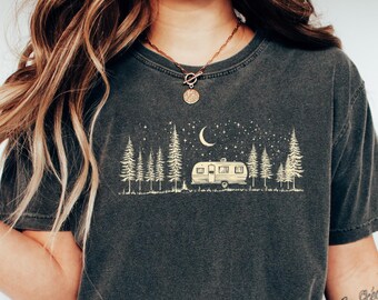 May include: Dark gray t-shirt featuring a camping scene with a camper, trees, moon, and stars. The shirt is paired with blue jeans and white slip-on shoes. The overall theme is outdoor adventure and travel.