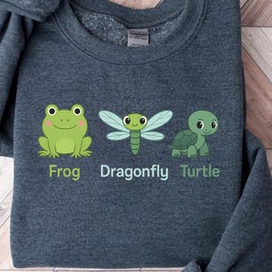 May include: A dark gray sweatshirt with a frog, dragonfly, and turtle graphic. The text "Frog, Dragonfly, Turtle" is printed below the graphic.