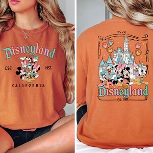 Puede incluir: Camiseta naranja con un gr&aacute;fico de Disneyland con Mickey Mouse, Minnie Mouse, Donald Duck, Goofy y Pluto. El texto de la camiseta dice "Disneyland Est. 1955 California".