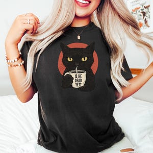 May include: Black t-shirt with a graphic of a black cat holding a coffee mug that says "Is he dead yet?"