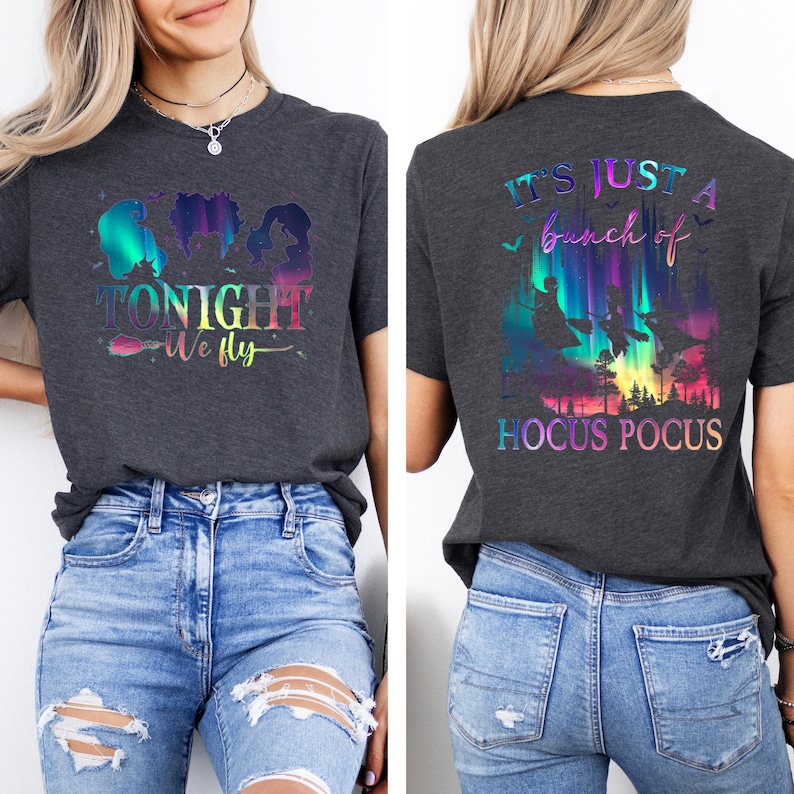 May include: Dark gray t-shirt with a colorful graphic featuring silhouettes of three witches and the text "TONIGHT WE FLY" on the front. The back of the shirt has the text "IT'S JUST A bunch of HOCUS POCUS" with a colorful witchy scene.
