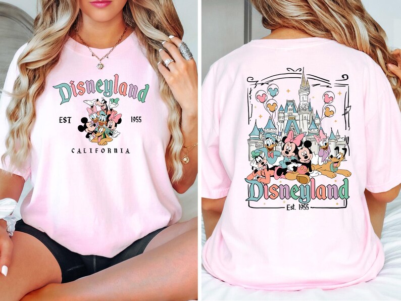 Puede incluir: Camiseta rosa con un gr&aacute;fico de Mickey Mouse y sus amigos frente a Disneyland. La parte delantera de la camiseta dice "Disneyland Est. 1955 California". La parte trasera de la camiseta tiene un gr&aacute;fico de Mickey Mouse y sus amigos frente al Castillo de la Bella Durmiente con el texto "Disneyland Est. 1955".
