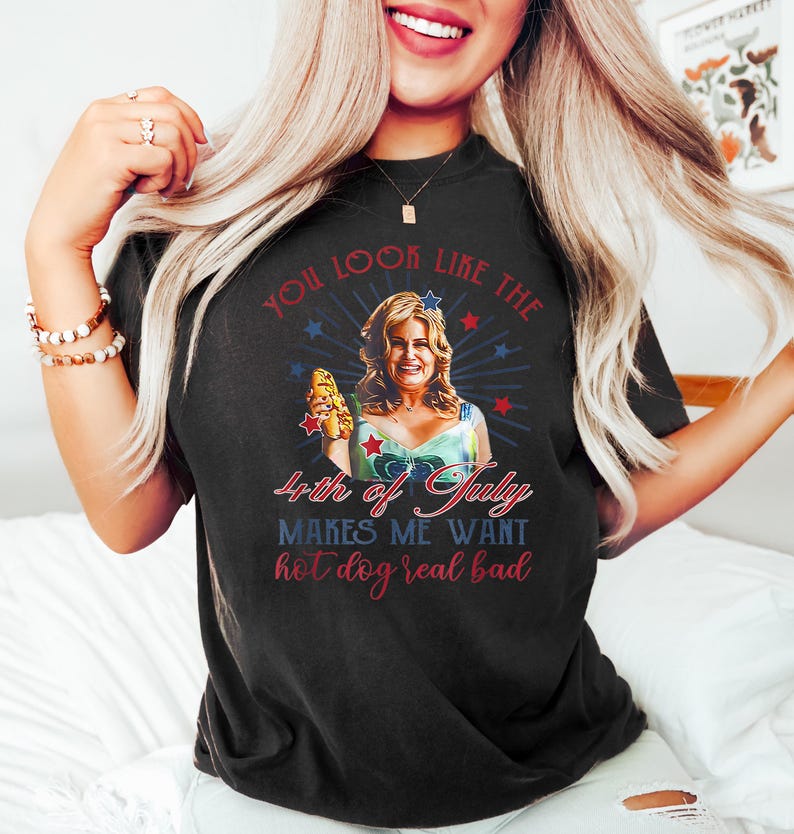 May include: A black t-shirt with a graphic of a woman holding a hot dog. The text on the shirt reads "You look like the 4th of July makes me want hot dog real bad."