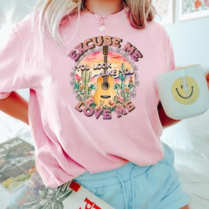 May include: Pink t-shirt with a graphic of a guitar, cacti, and the text "Excuse Me You Look Like You Love Me".
