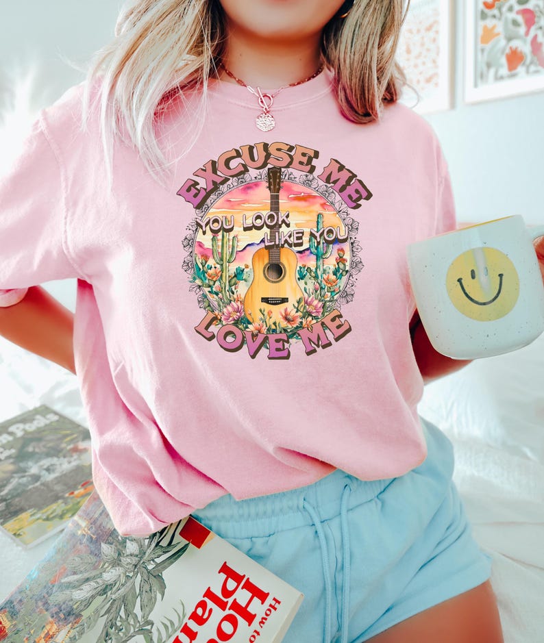 May include: Pink t-shirt with a graphic of a guitar, cacti, and the text "Excuse Me You Look Like You Love Me".