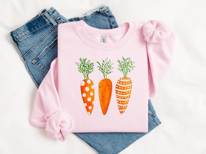 Puede incluir: Una sudadera rosa con un gr&aacute;fico de tres zanahorias naranjas con lunares blancos y rayas. Las zanahorias tienen hojas verdes.