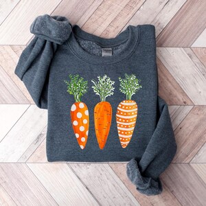 Puede incluir: Una sudadera gris oscuro con un dise&ntilde;o de tres zanahorias naranjas con lunares blancos y hojas verdes.