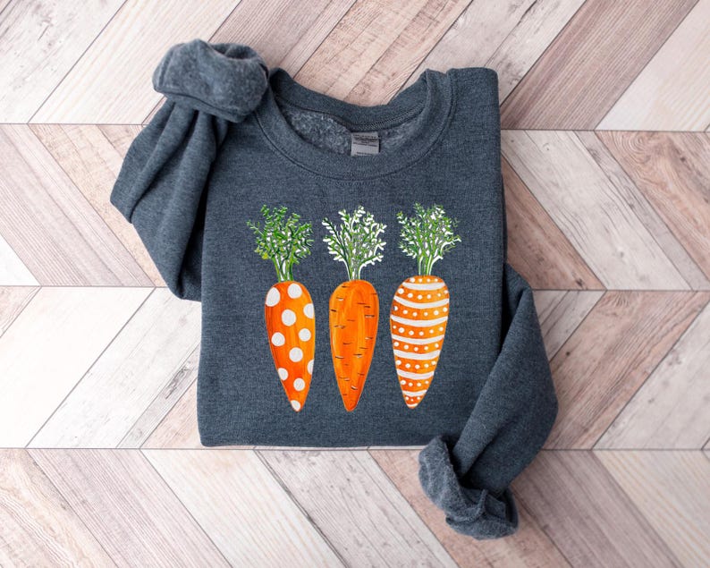 Puede incluir: Una sudadera gris oscuro con un dise&ntilde;o de tres zanahorias naranjas con lunares blancos y hojas verdes.