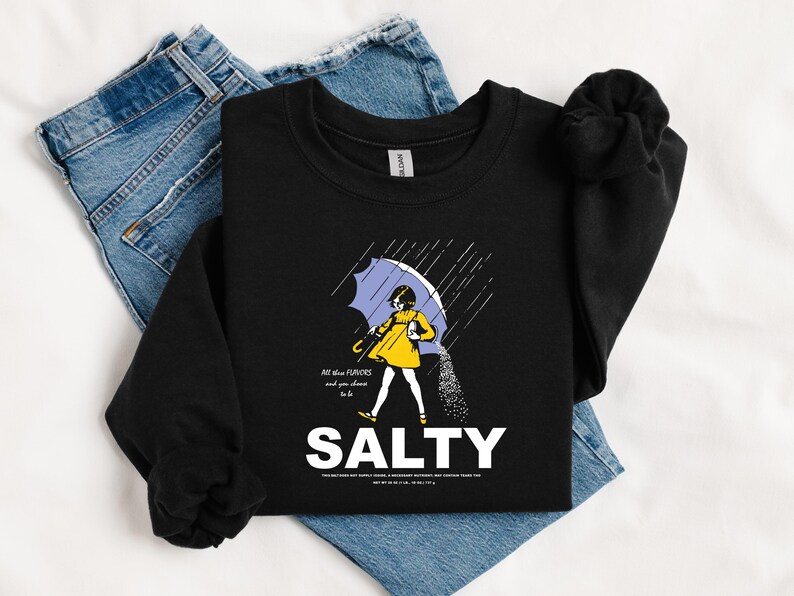 May include: Black sweatshirt with a graphic of a person under a blue umbrella, with the word "SALTY" in large white letters. The person is wearing a yellow coat and the image includes the text "All the flavors and you choose to be".