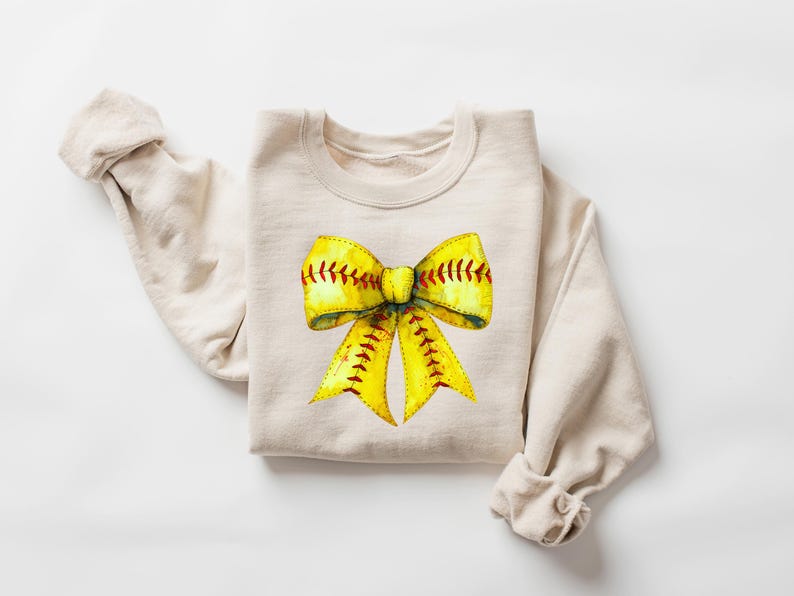 K&ouml;nnte beinhalten: Ein beiger Pullover mit einem gelben und roten Softball-Schleifendesign.