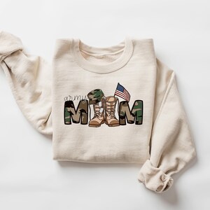 May include: A beige sweatshirt with a camouflage print that reads "army mom" with a pair of boots and a small American flag.