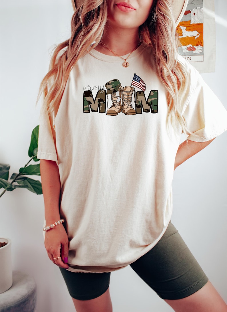 May include: A white t-shirt with the text "army mom" in camouflage print with a pair of army boots and a small American flag.