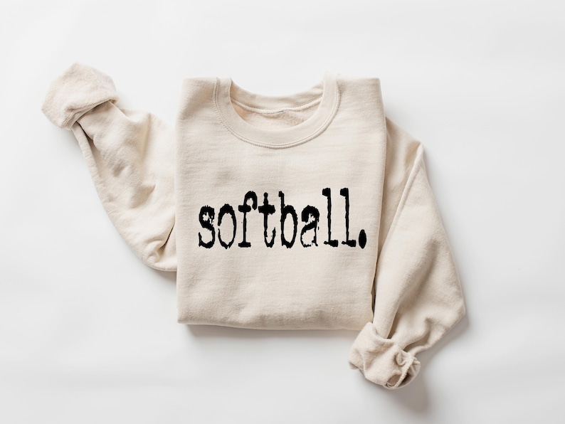 K&ouml;nnte beinhalten: Ein beiger Pullover mit dem Wort "Softball" in Schwarz auf der Vorderseite.