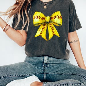 K&ouml;nnte beinhalten: Ein anthrazitfarbenes T-Shirt mit einem gelben Softball-Schleifen-Motiv. Die Schleife ist mit rotem Garn gestickt und hat einen Aquarell-Effekt.